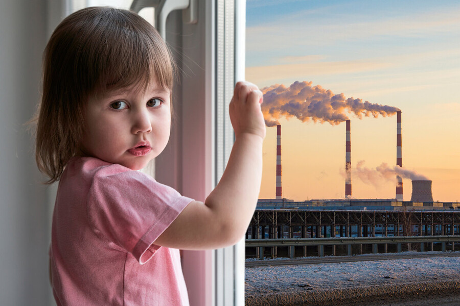 Young child looking out window at industrial smokestacks